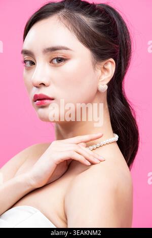 Une jeune femme avec un collier de perles pose avec sa main sur son épaule. Banque D'Images