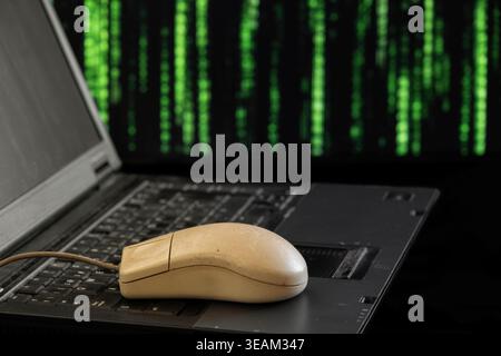 une souris série vintage et usée, des années 1990, placée au-dessus d'un clavier d'ordinateur portable avec un fond matriciel Banque D'Images