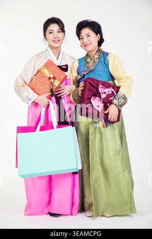 Deux femmes, une jeune et une âgée, habillées en Hanbok coréen traditionnel, tenant des coffrets cadeaux et souriant à la caméra. Banque D'Images