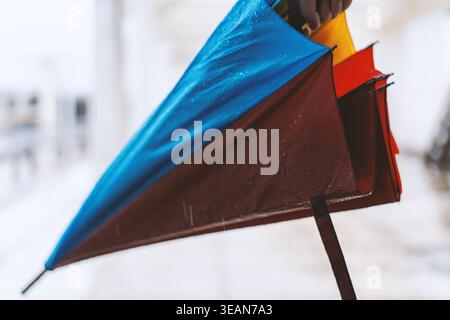 Parapluie humide coloré tenu à la main pendant la journée pluvieuse d'hiver, gros plan avec un fond enneigé flou Banque D'Images