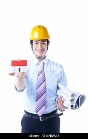 Un jeune ingénieur tient une petite maquette d'une maison et un ensemble de plans. Banque D'Images