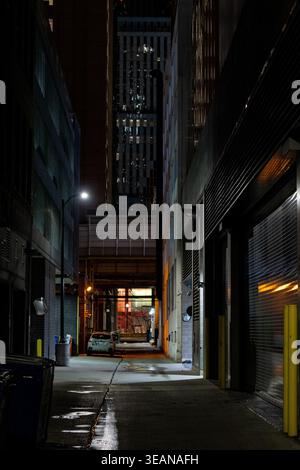 Vue d'ambiance dans une étroite ruelle urbaine la nuit entre les bâtiments, avec une voiture garée, l'éclairage ambiant de la rue, la perspective noire en un point Banque D'Images