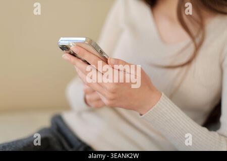 Femme utilisant smartphone à l'intérieur gros plan. Gros plan d'une femme tenant et utilisant un smartphone assis à l'intérieur, montrant la communication moderne Banque D'Images