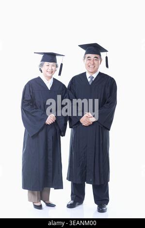 Deux personnes asiatiques âgées, probablement diplômés ou étudiants, se tiennent côte à côte, tous deux portant des regalia académiques traditionnels. Banque D'Images