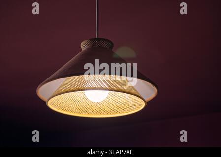 La lampe suspendue tissée diffuse une lumière chaude. Lumière douce projette un motif doux contre le plafond sombre. Le design moderne allie texture et chaleur ambiante Banque D'Images