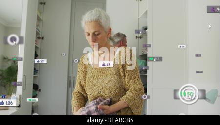 Tenant le vêtement plié, femme mature en tricot de moutarde organisant le placard à la maison avec des étiquettes AR. Garde-robe, organisation, stockage, ménage, intérieur, m Banque D'Images