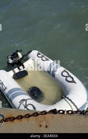 Vue à angle élevé d'un canot gonflable blanc avec un moteur hors-bord flottant dans l'eau turquoise claire alors qu'il est amarré à une jetée en béton avec un met rouillé Banque D'Images