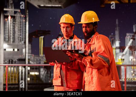 Équipe d'ingénieurs inspectant l'activité de la plate-forme de forage la nuit, assurant une extraction efficace du pétrole et du combustible naturel à partir de la plate-forme offshore. Travailler ensemble sur la production de pétrole pour l'industrie. Banque D'Images