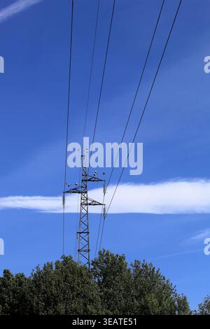 Vitorino das Donas, Portugal - 26 mars 2026 : vue lointaine d'un pylône électrique en treillis d'acier s'élevant au-dessus de la cime verte des arbres contre un SK bleu vif Banque D'Images