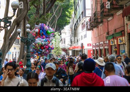 Grand groupe de personnes marchant dans une rue animée dans le centre historique de Puebla, entouré d'une architecture ancienne et de ballons colorés. Banque D'Images
