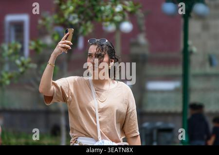 Une jeune femme avec des lunettes de soleil sur la tête tient son téléphone portable pour prendre une photo dans un parc. Banque D'Images