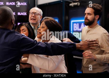 Les acheteurs de gens deviennent fous pour se rendre au magasin d'abord afin d'obtenir les meilleures offres pendant les ventes du Black Friday. Foule en colère de clients se battant avec l'agent de sécurité en attendant à l'entrée du centre commercial Banque D'Images
