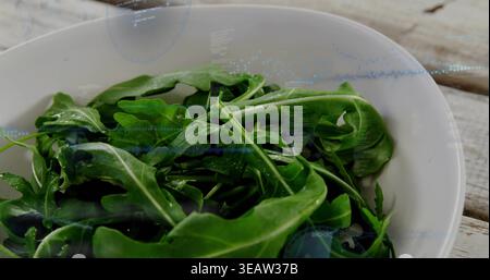 Affichage bol en céramique blanc tenant des feuilles fraîches de roquette dans la cuisine sur une table en bois, des gouttelettes d'eau Banque D'Images