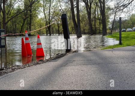Le sentier et la route du parc ont été inondés après de fortes pluies avec des cônes orange de circulation et une barrière de marquage de l'accès restreint, l'eau couvrant le sol et les arbres à l'intérieur Banque D'Images
