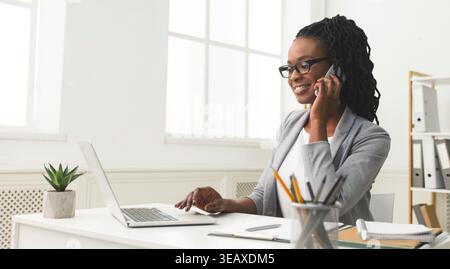 Femme professionnelle s'engage dans le travail tout en parlant au téléphone dans le cadre moderne de bureau Banque D'Images