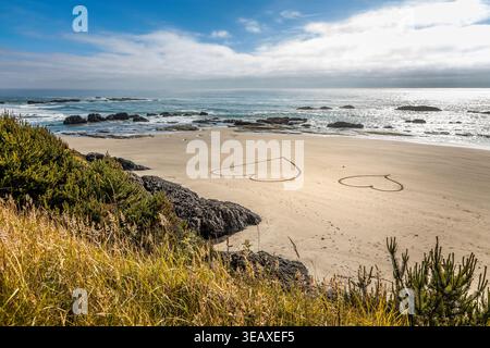 Côte romantique de l'Oregon avec plage de sable, falaises rocheuses et deux cœurs dessinés à la main près des vagues de l'océan Banque D'Images