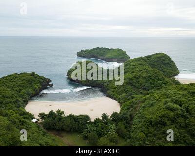 Vue aérienne de la plage isolée nichée entre les collines verdoyantes et le vaste océan, un paradis caché, Sedahan Beach, Gunungkidul Regency, spécial Banque D'Images