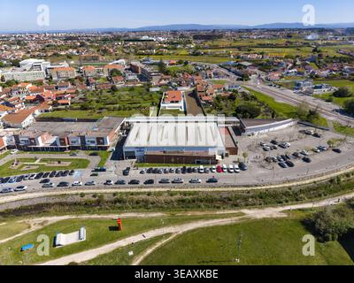 Vue aérienne d'un bâtiment avec un grand parking, entouré de maisons et de champs verdoyants à Espinho, Portugal. Banque D'Images