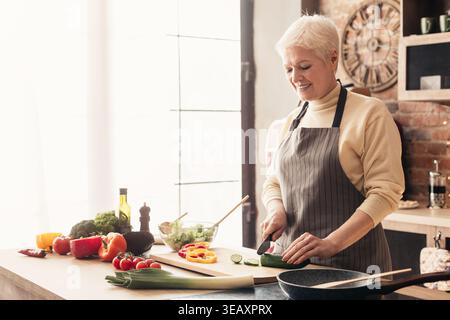 Femme senior préparant des légumes frais pour un repas sain dans une cuisine confortable Banque D'Images