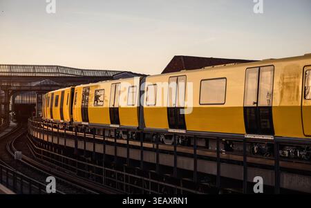 Train de métro jaune sur des voies surélevées au coucher du soleil. Une vue latérale d'un train de banlieue moderne courbant le long de voies élevées pendant l'heure dorée. Banque D'Images