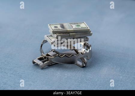 Une pile de billets de cent dollars utilisés comme appât sur un piège en acier. Cupidité financière, pièges de dette, escroqueries d'argent, et concept d'investissement à haut risque. Banque D'Images
