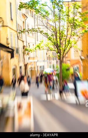 Les gens se déplacent le long d'une rue animée avec des magasins, des bâtiments et des arbres verts Banque D'Images
