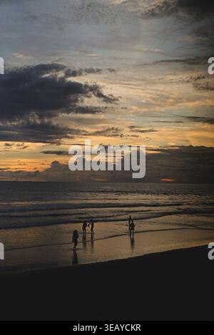 Groupe de personnes sur le sable humide au coucher de soleil tropical vif, Canggu, Bali Banque D'Images