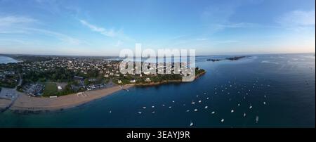 Vue aérienne d'une plage de sable rencontrant les eaux tranquilles et ponctuées de bateaux, avec la ville s'étendant à l'intérieur des terres, Carantec, Bretagne, France. Banque D'Images