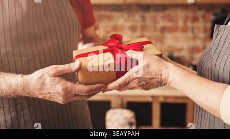 Échange de cadeaux entre deux personnes dans un cadre Cozy Kitchen lors d'une occasion festive Banque D'Images