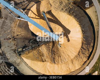 Vue aérienne d'un amas colossal de copeaux de bois baigné de lumière chaude du soleil, contrasté par le bleu frais de la grue industrielle, Cacia, Portugal. Banque D'Images