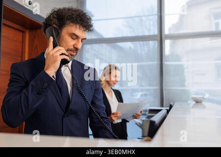 Réceptionniste parlant au téléphone de bureau avec une employée en arrière-plan Banque D'Images