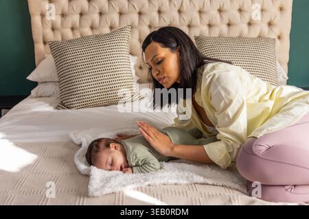 Mère et nourrisson afro-américains, maman agenouillée sur le lit penchée sur le nourrisson endormi près de la tête de lit Banque D'Images