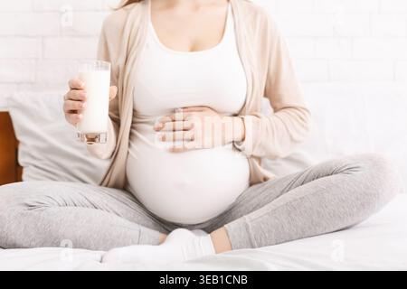 Femme enceinte profitant d'un verre de lait tout en étant assis confortablement sur un lit Banque D'Images