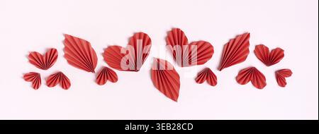 Bannière Web faite de coeurs bouclés rouges et de feuilles sur une vue de dessus de fond rose Banque D'Images