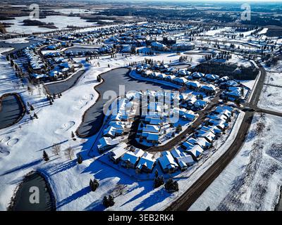 Couvertures de neige maisons et routes dans cette vue aérienne de banlieue. Des rangées de toits enneigés forment un aménagement de quartier tranquille. Étangs et voies navigables ouvertes Banque D'Images