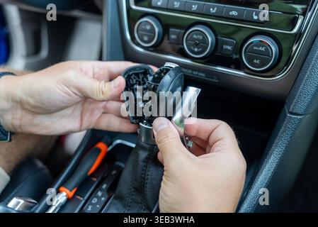 Mains réparant le pommeau de changement de vitesse automatique de voiture à l'intérieur du véhicule, gros plan du sélecteur démonté, de l'entretien automatique et du concept de réparation. Banque D'Images