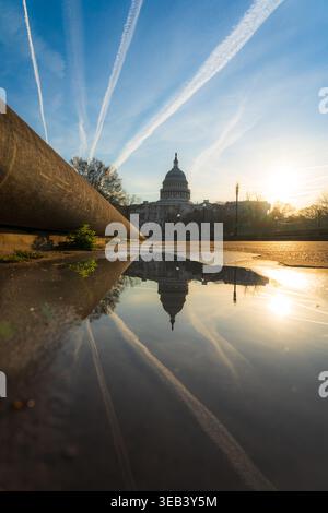 Vue du bâtiment du Capitole des États-Unis reflétée dans une flaque de pluie au lever du soleil avec des traînées à travers le ciel bleu à Washington, District de Columbi Banque D'Images