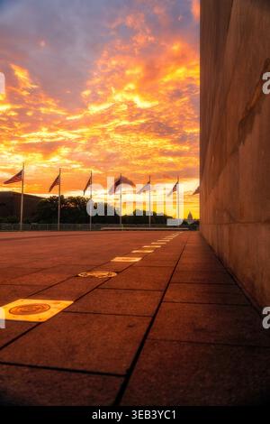 Vue de la base du Washington Monument avec des drapeaux américains agitant contre un ciel de coucher de soleil orange et le lointain bâtiment du Capitole à Washington, Di Banque D'Images
