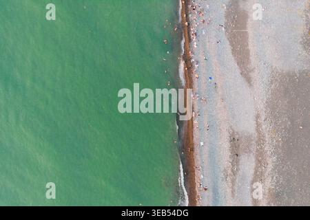 Vue aérienne de dessus de l'eau de mer turquoise et plage de galets avec des gens. Vacances d'été, style de vie côtier, fond de nature minimaliste et tourisme conc Banque D'Images
