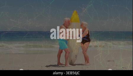 Tenue de planche de surf, couple senior debout sur le rivage, boxers turquoise et maillot de bain noir bordure bleue Banque D'Images
