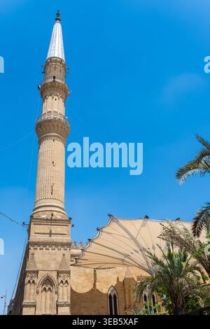 Vue sur le minaret orné de la mosquée Imam Al-Hussein avec une grande canopée blanche et des palmiers sous un ciel bleu clair au Caire, Egypte. Banque D'Images