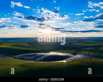 Les panneaux solaires couvrent une grande partie du terrain dans une zone rurale. Le soleil se couche, projette de la lumière à travers le champ, tandis que les nuages se déplacent dans le ciel. Banque D'Images