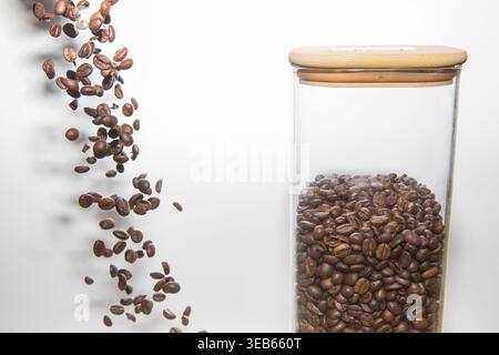 Grains de café tombant dans un pot en verre sur fond blanc concept de nourriture et de fraîcheur Banque D'Images