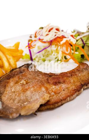 Découpée à l'emporte-pièce de porc steak avec frites et salade de légumes mis dans le plat blanc sur blanc isolé. Banque D'Images