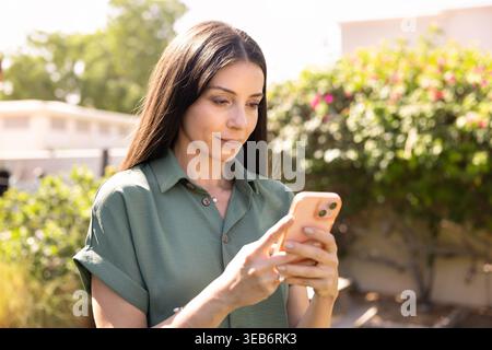 Femme adulte concentrée utilisant un smartphone debout à l'extérieur Banque D'Images