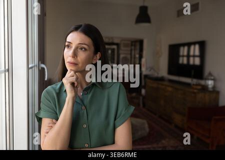 Femme debout près de la fenêtre pensant aux préoccupations de la vie Banque D'Images