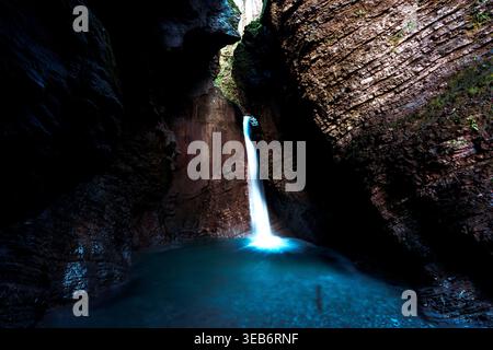 Vue sur la cascade de Kozjak en cascade dans une piscine turquoise dans une caverne de calcaire sombre en Slovénie. Banque D'Images