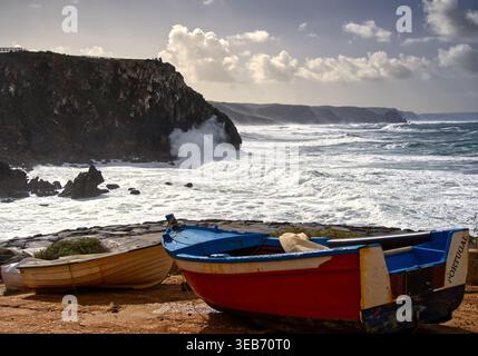 Les bateaux de pêche reposent sur une côte altérée tandis que de puissantes vagues s'écrasent contre les falaises de la côte atlantique portugaise, représentant un réseau local côtier accidenté Banque D'Images