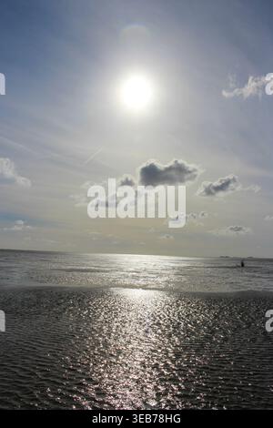 La lumière du soleil scintille sur le sable humide et la mise en commun de l'eau de la mer des wadden avec un soleil brillant dans le ciel Banque D'Images