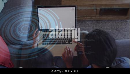 Regarder le duo mentor-étudiant coder et pointer sur le canapé gris à la maison avec ordinateur portable, HUD, coussin rouge Banque D'Images
